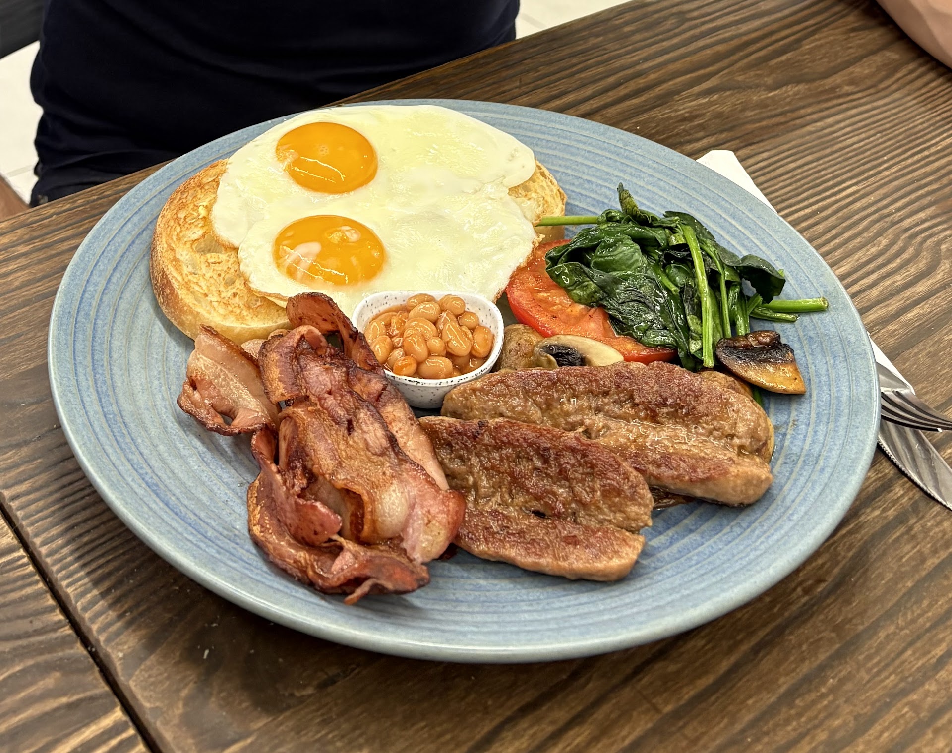 Big breakfast with fried eggs, bacon, sausage, spinach, tomato, and beans